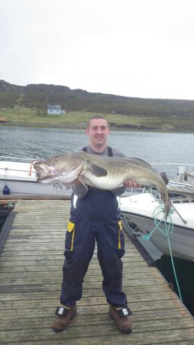 a man holding a fish on a dock at Hotel Repvåg in Repvåg