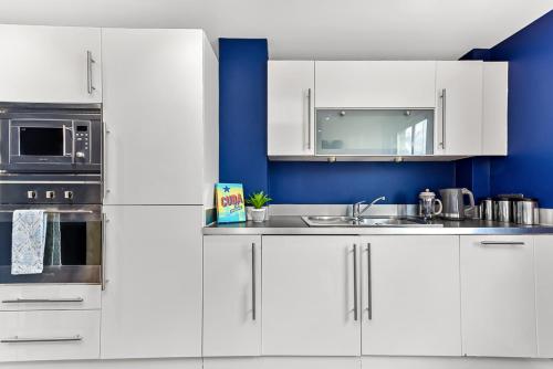 una cucina con armadi bianchi e parete blu di Spacious Cosy 2 Bed Flat, Central London a Londra