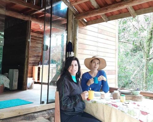 deux femmes assises à une table avec des tasses de café dans l'établissement Cabanas Pousada Esmeraldas, à Annitapolis