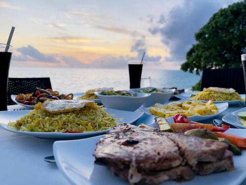 a table with plates of food on a table with the ocean at Thoddoo Beach Holiday in Thoddoo