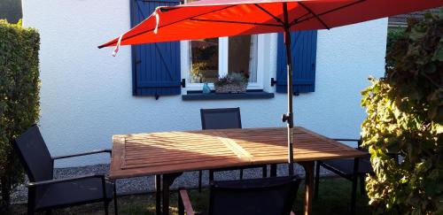 una mesa de madera con una sombrilla roja frente a una casa en Les Ondines, en Estréelles