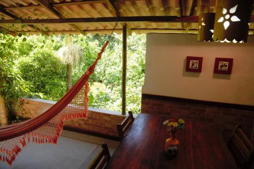 a room with a table and a hammock in a house at Casa Flôr - Beira rio Centro de Lumiar in Lumiar