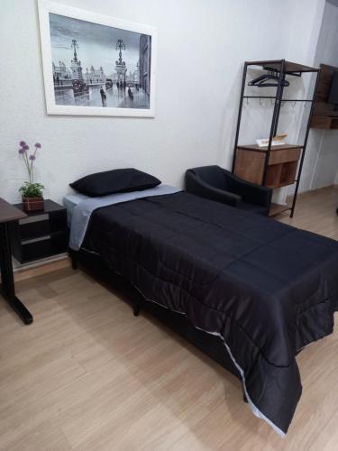 ein Schlafzimmer mit einem schwarzen Bett und einem Stuhl in der Unterkunft FLAT LOCAÇÃO TEMPORADA NO CENTRO DE ITAPIRA in Itapira