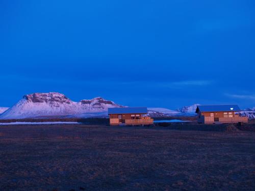 two houses in a field with a mountain in the background at Vestri Pétursey in Vestri Pétursey