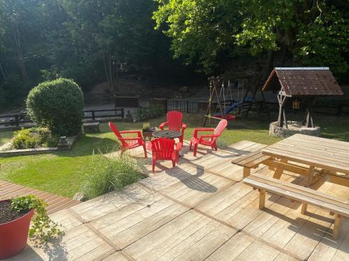 a wooden deck with red chairs and a picnic table at Le Gîte des Platanes in Spa