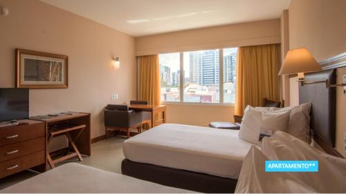 a hotel room with a bed and a desk and a window at Vila Galé Salvador in Salvador