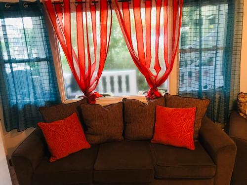a couch with red pillows in front of a window at HCEAS villa is 5 min fr. airport & to the beaches in Bon Accord