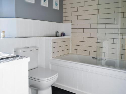 a white bathroom with a toilet and a bath tub at The Nook in Mealsgate