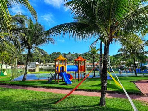 a playground with a slide in a park with a palm tree at JL Temporadas - Quarto Portobello Park Hotel in Porto Seguro