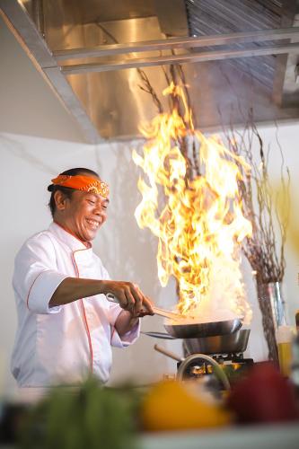 a man cooking food in a pan with flames at HARRIS Hotel and Conventions Denpasar Bali in Denpasar