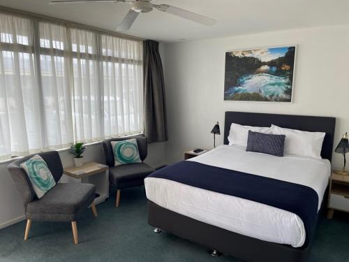 a bedroom with a large bed and two chairs at Academy Motor Inn in Tauranga