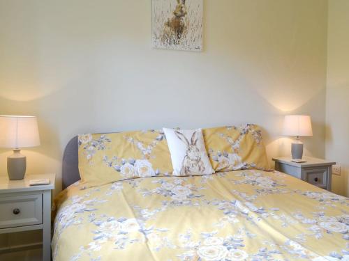 a bed with a yellow comforter and two lamps at Eagles Cottage in Corston