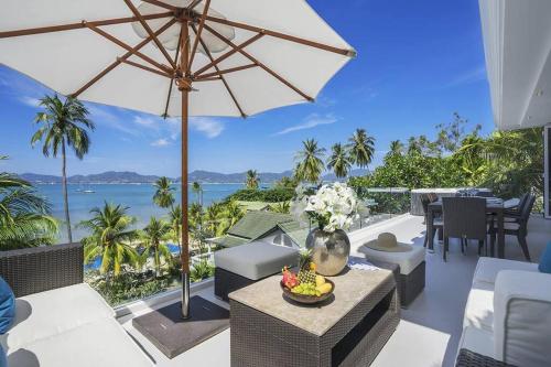 a patio with a table and an umbrella and the ocean at Villa Nirvana - Beachfront Tropical Chic 4BR Haven in Cape Panwa, Phuket in Ban Ao Makham