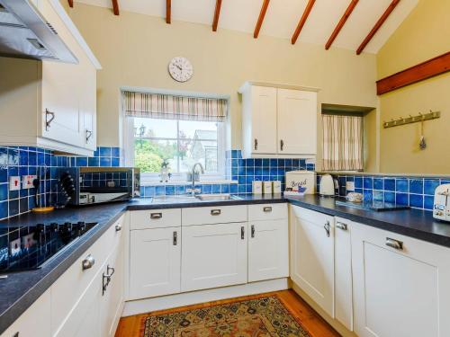 una cocina con armarios blancos y una pared de azulejos azules en Beudy - Uk31388, en Caeathro