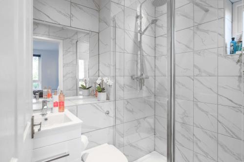 La salle de bains blanche est pourvue d'une douche et d'un lavabo. dans l'établissement LiveStay-4 Bed London Townhouse, Private Terrace, Parking, à Brentford
