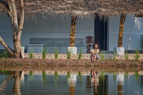 a woman sitting next to a body of water at Xandari Pearl Beach Resort in Mararikulam