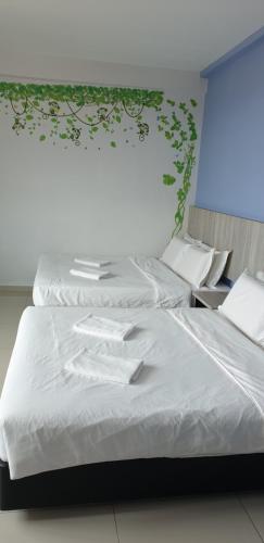 two beds in a room with white sheets and plants on the wall at 56 HOTEL in Mentekab