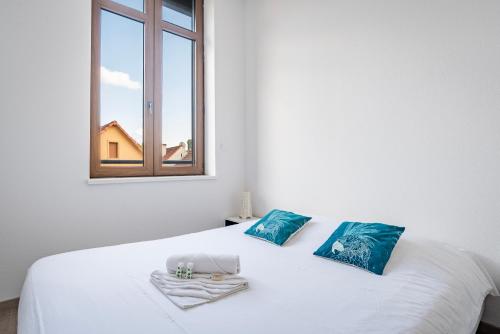 Cama blanca con almohadas azules y ventana en Le Manoir de Cyrielle - WIFI - 20 min centre ville de Strasbourg, en Bischheim