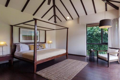 um quarto com uma cama de dossel e uma cadeira em StayVista at Bella Aquila with Pvt Pool & Lawn - Parra NorthGoa em Anjuna