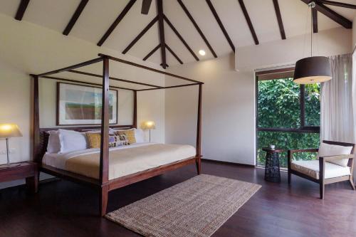 a bedroom with a canopy bed and a chair at StayVista at Bella Aquila with Pvt Pool & Lawn - Parra NorthGoa in Anjuna