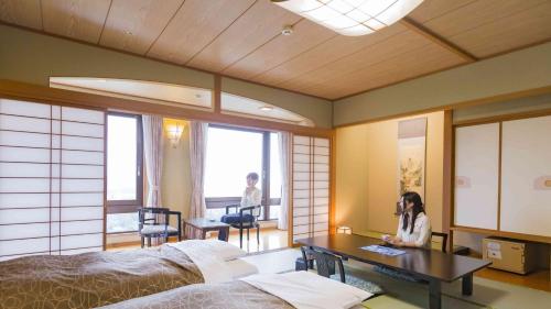 a woman is sitting at a desk in a bedroom at Hotel Morinokaze Oshuku in Shizukuishi