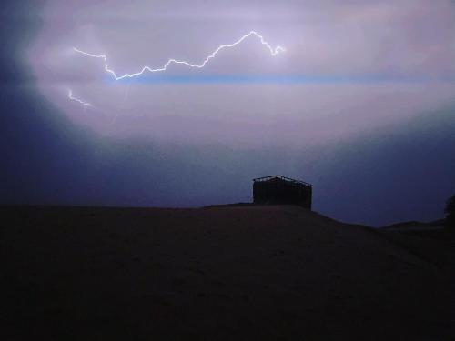 a lightning storm in the sky with a building on a hill at Merzouga Paradise Luxury Camp in Merzouga