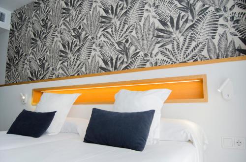 a bedroom with a white bed with a black and white wallpaper at Hotel Anfora Ibiza in Es Cana