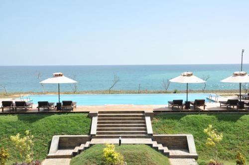 a pool with chairs and umbrellas and the ocean at Laya Safari Resorts & Spa in Yala