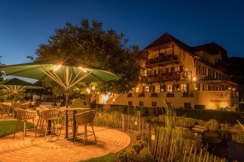 a table with chairs and an umbrella in front of a building at Mosers Blume Relax & Genuss Hotel in Haslach im Kinzigtal