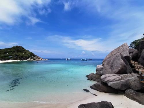 a beach with rocks and boats in the water at Nangyuan Island Dive Resort in Koh Tao