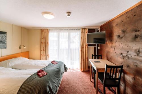 een hotelkamer met een bed, een bureau en een televisie bij Hotel Les Amis in Saas-Fee