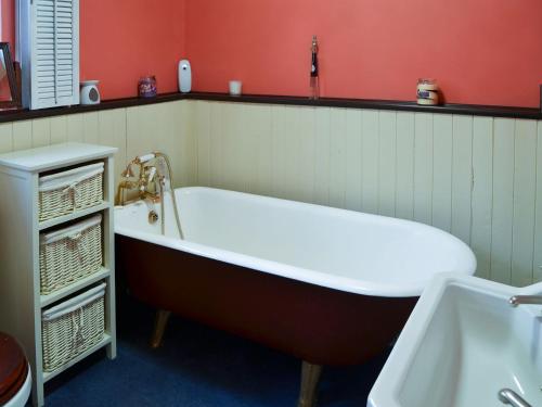 a bath tub in a bathroom with a red wall at Tattlepot Farmhouse in Tivetshall Saint Margaret