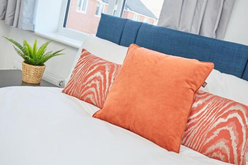 a white bed with two orange pillows and a plant at Cosy,Modern and Relaxing 3 bedroom house with parking in Manchester