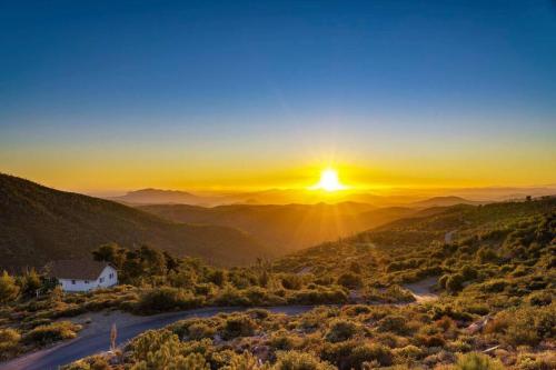 a sunset over the mountains with a house in the foreground at A LIVING CANVAS Amazing Lake View Custom Home in Julian