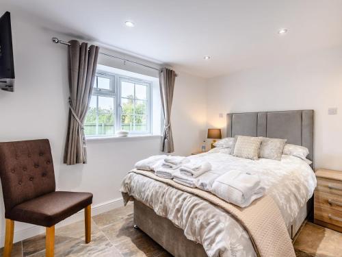 a bedroom with a bed and a chair and a window at Poppy Cottage in West Ashby