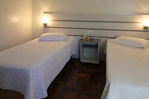 two beds in a hotel room with white sheets at Tri Hotel Xanxerê in Xanxerê