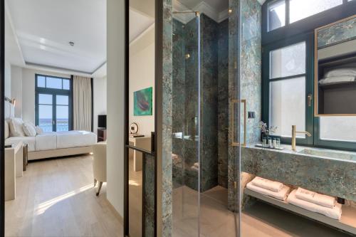 a bathroom with a glass shower and a bedroom at Grand Hotel Kalamata in Kalamata
