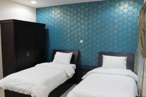 two twin beds in a room with blue wallpaper at شقق ليالي الشرق للوحدات 2 in Al Mubarraz