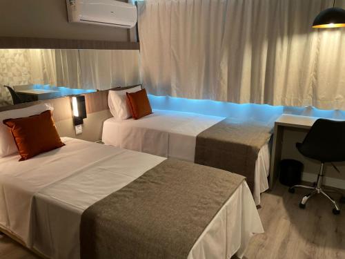 Habitación de hotel con 2 camas, escritorio y ventana en Logic Hotel Volta Redonda en Volta Redonda