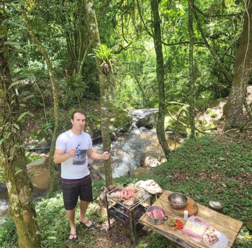 Un homme debout à côté d'une table de pique-nique à côté d'un ruisseau dans l'établissement Cabanas Pousada Esmeraldas, à Annitapolis