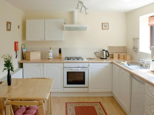 uma cozinha com armários brancos e um forno com placa de fogão em The Shippon em Lympsham