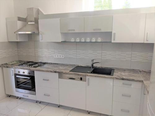 uma cozinha com armários brancos, um lavatório e um fogão em Marica Apartman em Balatonfenyves