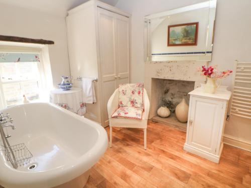 a bathroom with a tub and a chair and a fireplace at Clematis Cottage in Bakewell