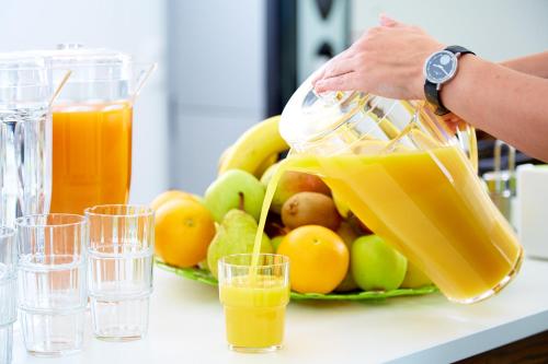 a person pouring orange juice into a bowl of fruit at Good Rooms GmbH Guntramsdorf in Guntramsdorf