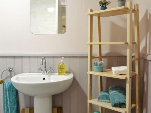 a bathroom with a sink and a shelf with towels at Arthurs Cottage in Edzell