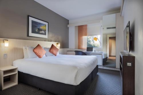 a hotel room with a large bed and a desk at ibis Auckland Ellerslie in Auckland