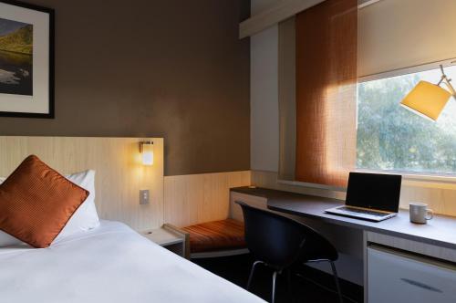 a hotel room with a bed and a laptop on a desk at ibis Auckland Ellerslie in Auckland