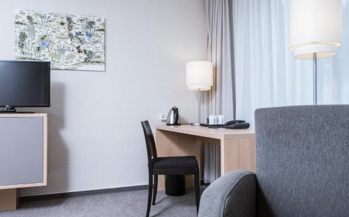 a hotel room with a desk with a chair and a television at Mercure Hotel Düsseldorf Neuss in Neuss