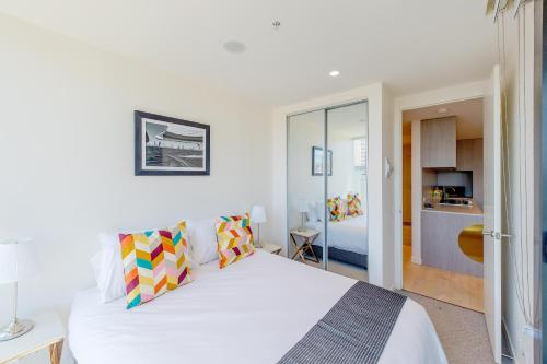 a bedroom with a large white bed and a kitchen at Realm Apartments by CLLIX in Adelaide