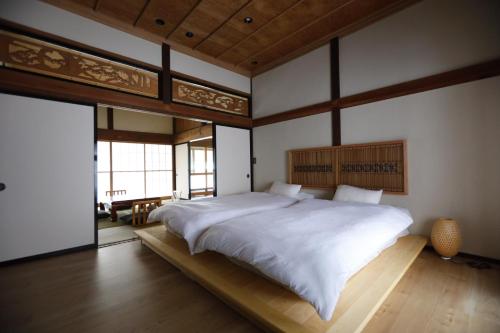 een slaapkamer met een groot wit bed met een houten hoofdeinde bij [貸切り] 220㎡ 月のワルツ 108年前の高級古民家 in Komoro